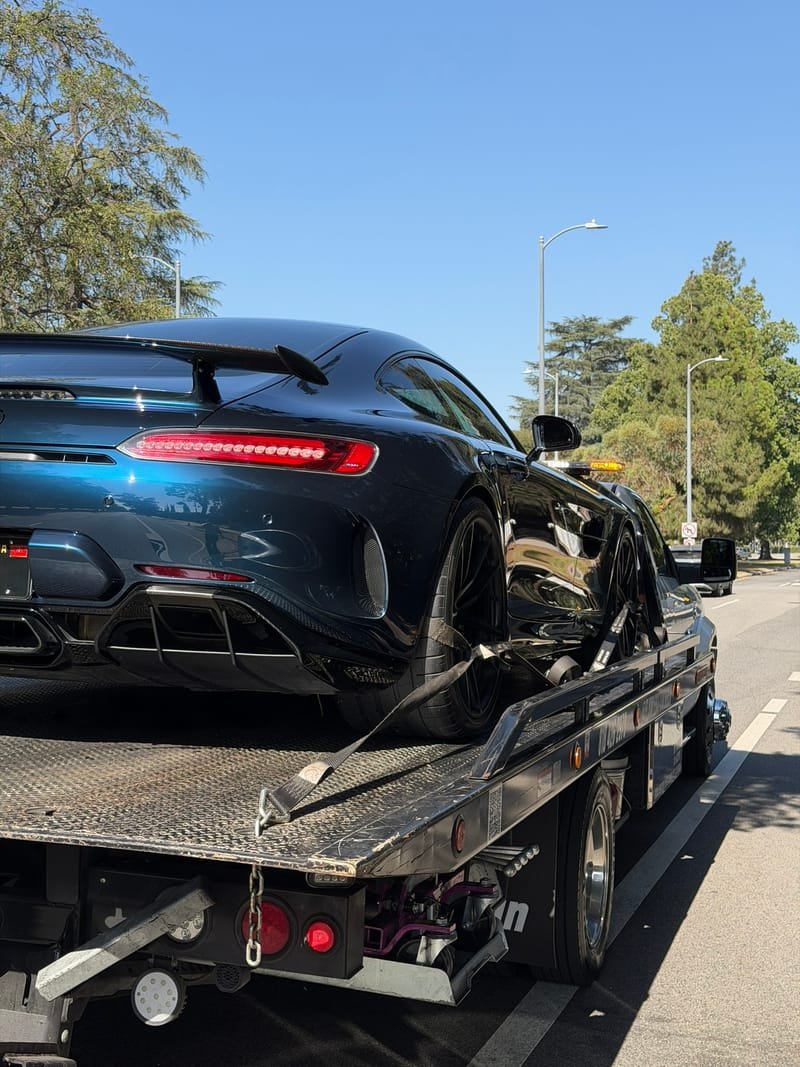 A blue Mercedes-AMG GT R loaded on a flatbed on a tree-lined Los Angeles street