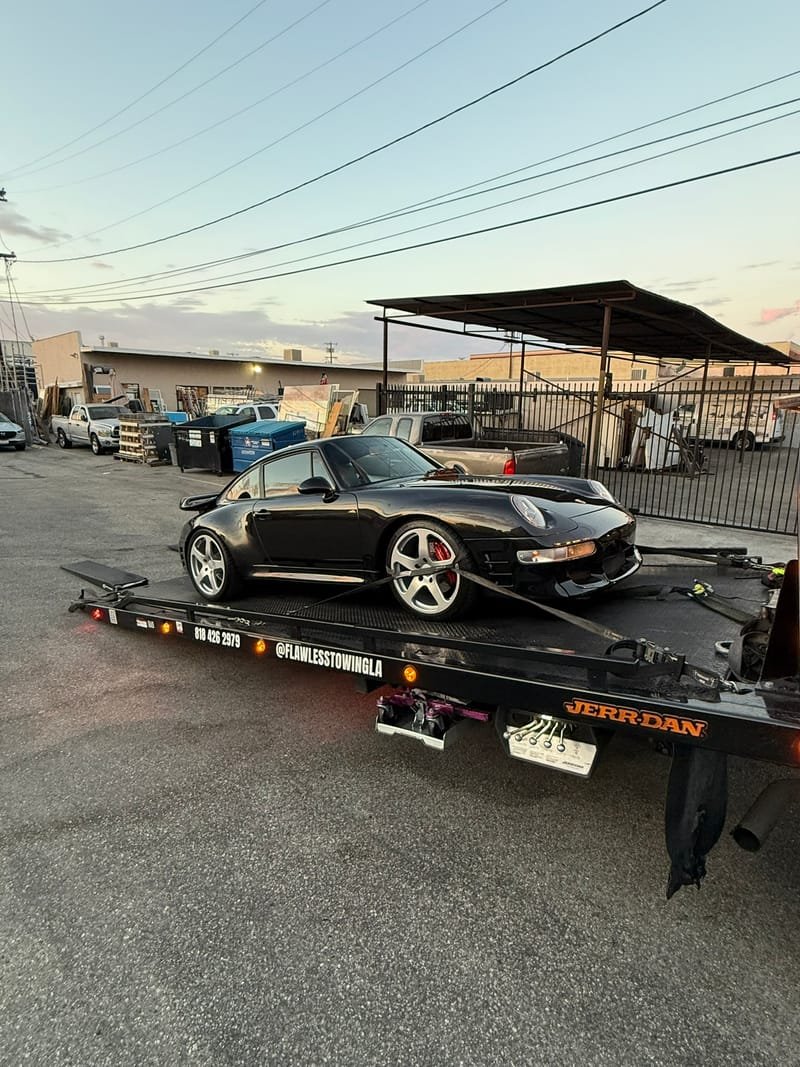 A black Porsche 911 993 Turbo on a Flawless Towing flatbed at dusk